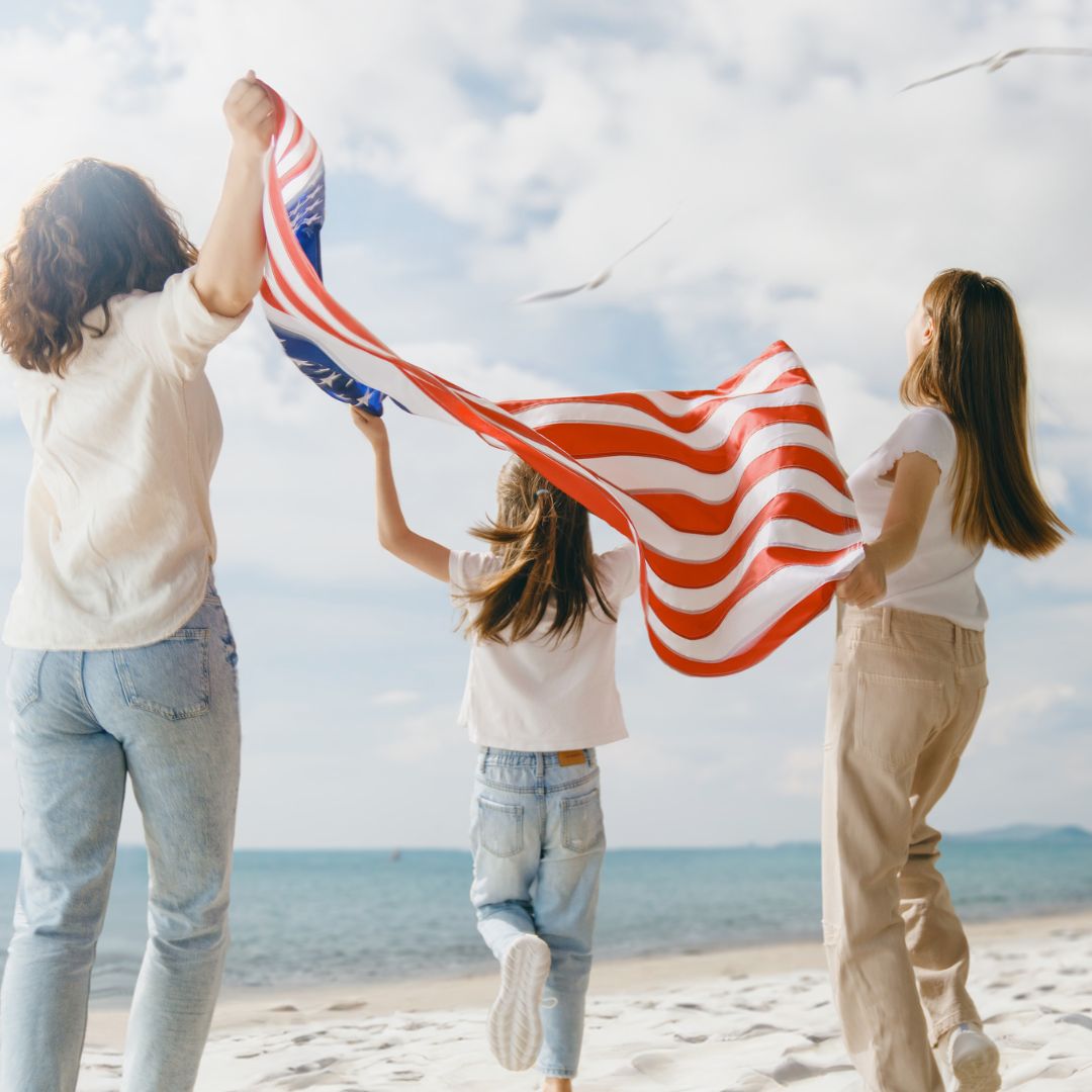 Family of 3 females on the beach waving a US flag